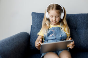 Menina mexendo em uma tela do tablet enquanto usa fones de ouvido.