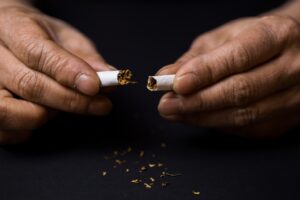 Um closeup nas mãos de alguém que está quebrando um cigarro ao meio, servindo como ilustração para a ideia de abandonar o tabaco.